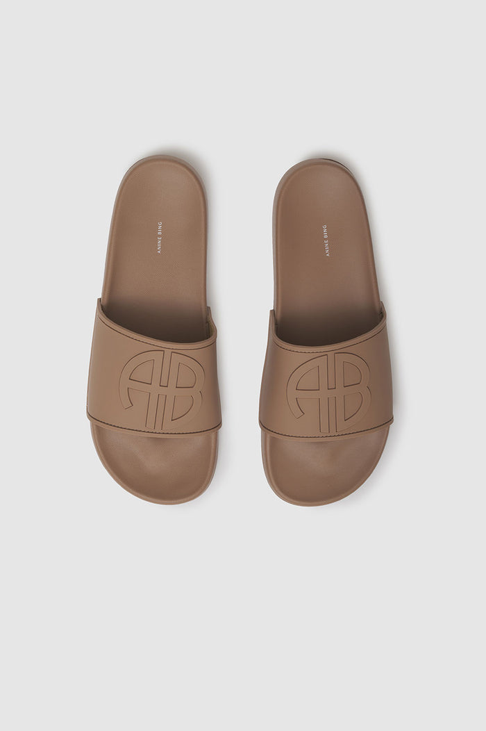 Camel-colored slides with a monogram design on the strap and a flat sole.