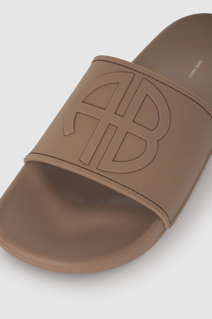 Camel-colored slide sandal featuring a large embossed monogram on the strap.